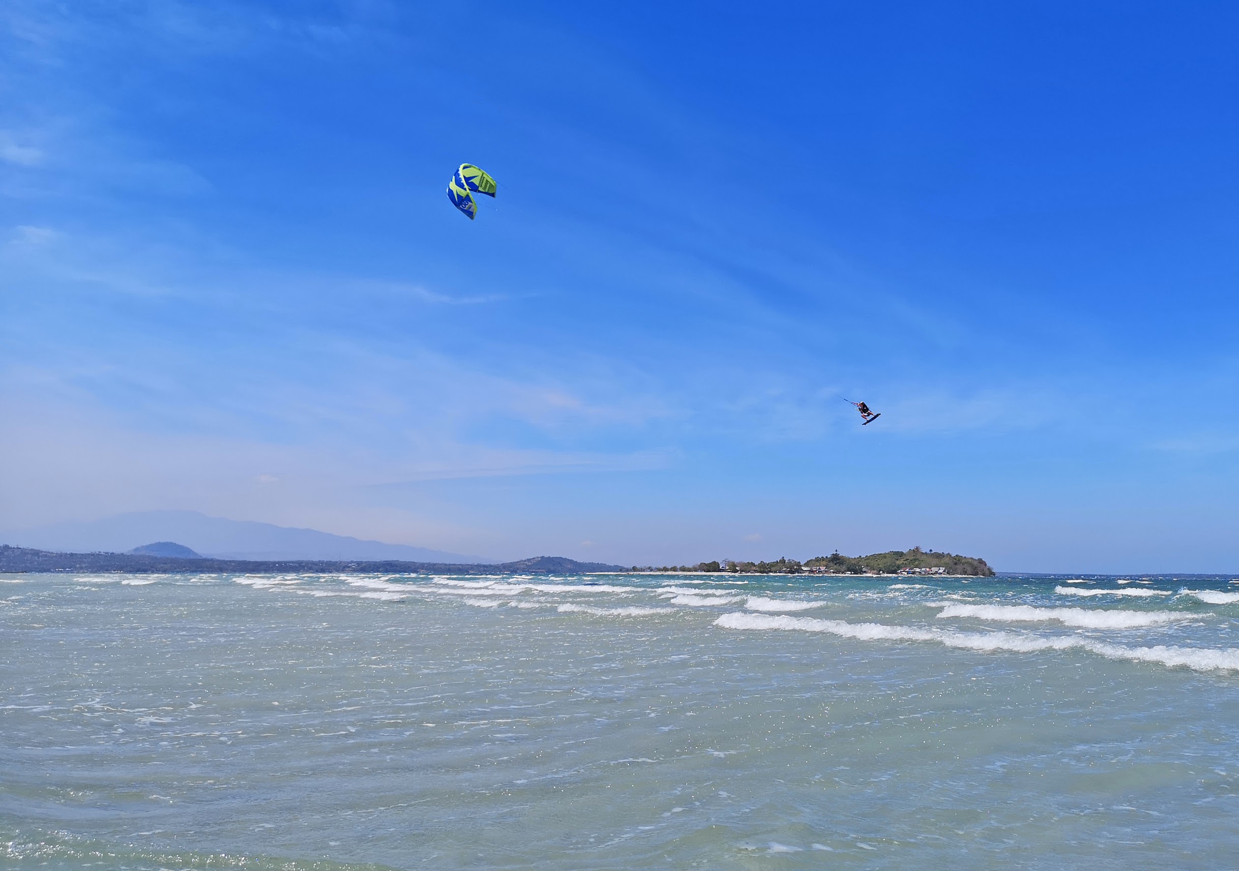 Kitesurfer sending a massive kiteloop over shallow lagoon in strong winds conditions in Sulawesi, Indonesia.