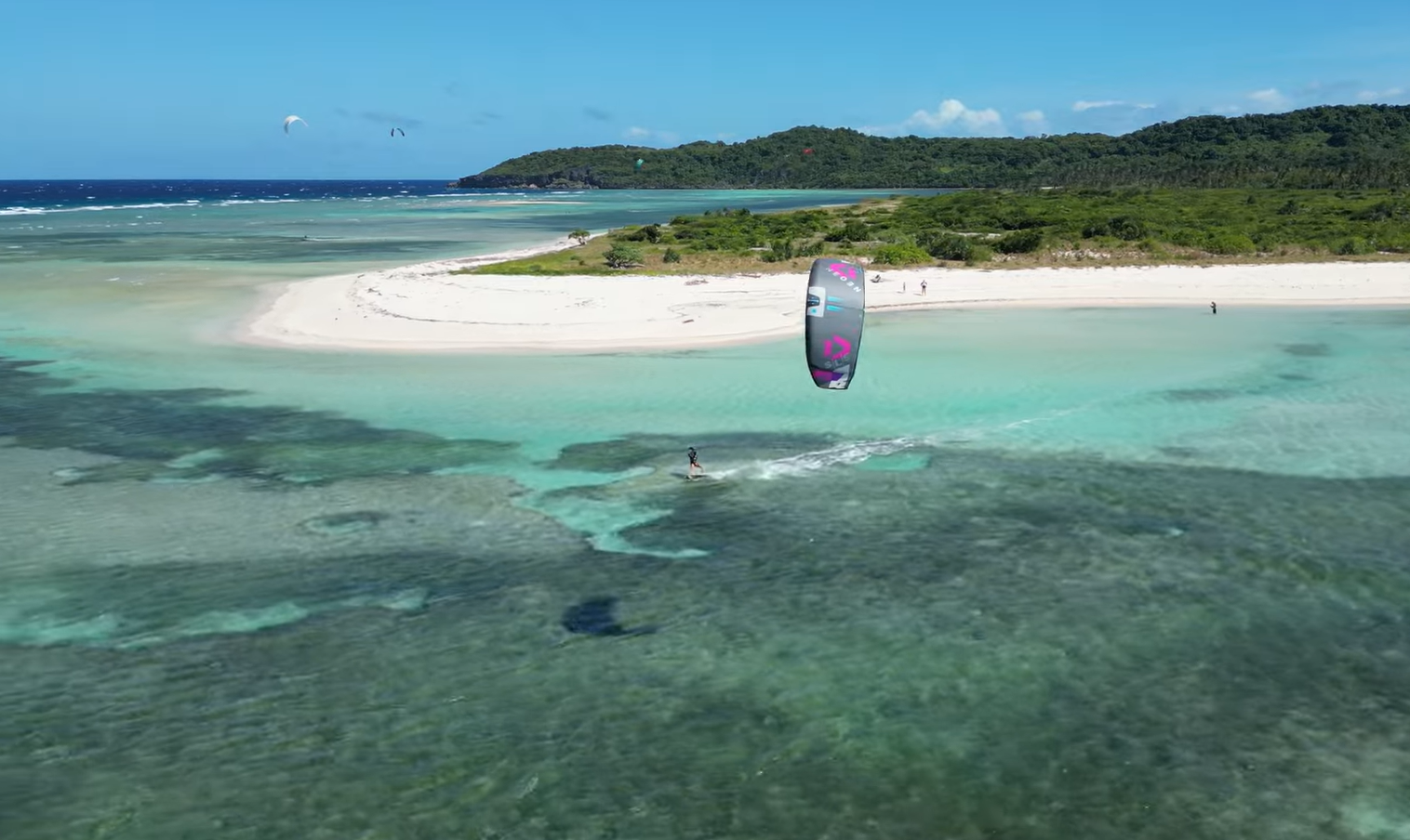 Kitesurfer riding across turquoise water near a sandbar at Bislig in Mindoro, Philippines.
