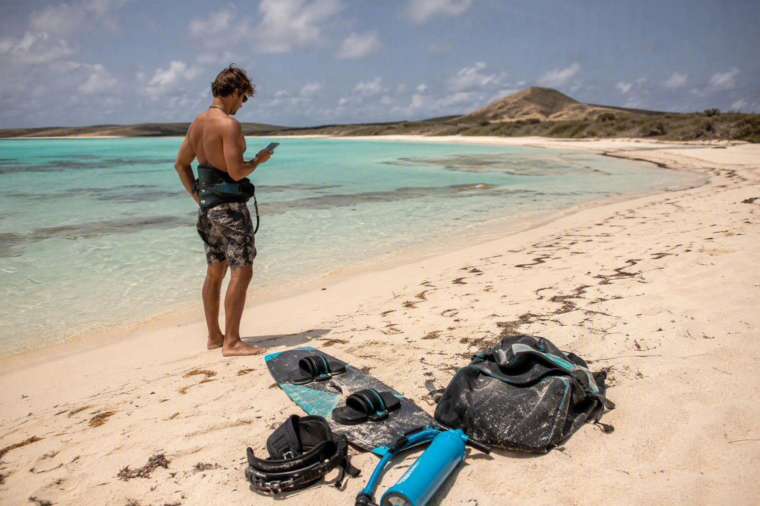 Kitesurfer checking wind forecast on a remote tropical beach beside a turquoise lagoon before a kitesurf session in Asia